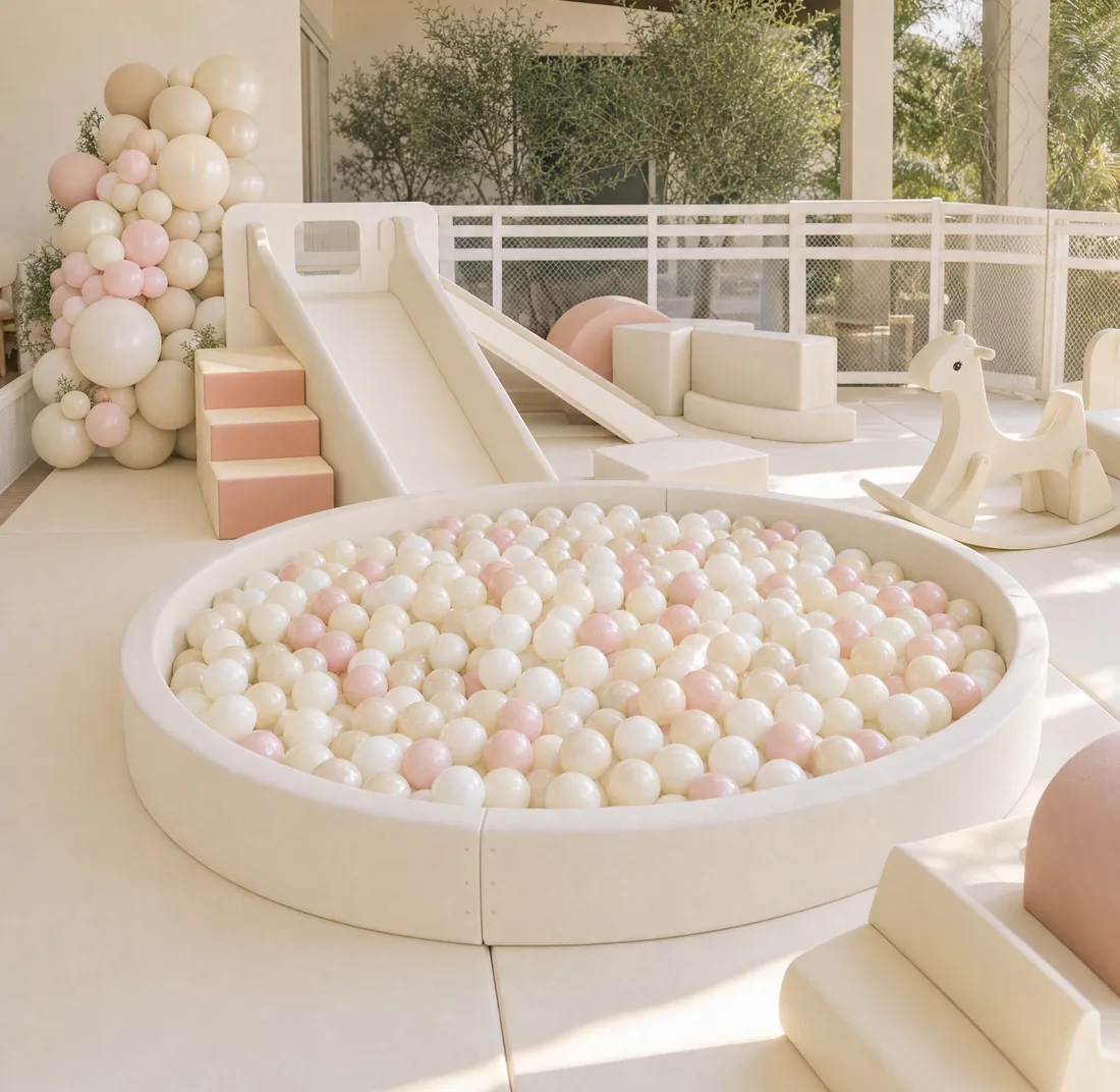 A cream soft play setup with a pearlescent ball pit, slide and balloon garland, staged for a party